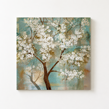 Load image into Gallery viewer, Square canvas wall art featuring a blossoming tree with white flowers and a brown trunk, painted against a textured teal and beige background, shown hanging on a light wall.