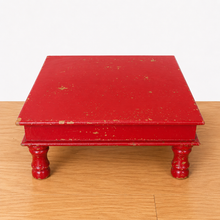 Load image into Gallery viewer, A small square red wooden box with four turned legs, shown on a light wood tabletop against a plain white background.