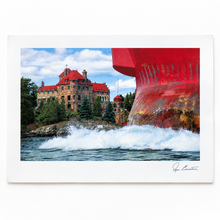 Load image into Gallery viewer, A matted photographic art print showing a large red ship hull cutting through white water next to a stone castle with a red roof under a blue sky. The print has a wide white border and a visible artist signature in the lower right corner.