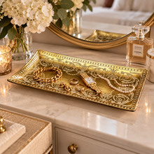 Load image into Gallery viewer, An ornate rectangular gold tray with embossed scrollwork sits on a marble vanity surface, styled with jewelry including a gold watch, bracelets, rings, and a pearl necklace. A Chanel perfume bottle, flowers, a mirror, and a candle are visible in the scene.