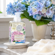 Charger l'image dans la galerie, Michel Design Works Wild Hydrangea hand wash in a clear pump bottle with a floral label, styled on a marble countertop with a vase of blue hydrangeas in the background.
