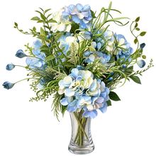 Charger l'image dans la galerie, A floral arrangement of light blue and white hydrangeas with green foliage, presented in a clear glass vase against a solid white background.
