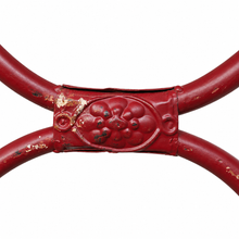 Load image into Gallery viewer, A close-up of a red metal table frame showing a decorative oval center with a grape motif and distressed paint showing the underlying gold-toned metal.
