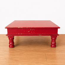 Load image into Gallery viewer, A small red wooden platform or low table with four turned legs, shown on a light wood floor against a plain white wall.
