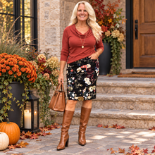 Load image into Gallery viewer, A woman stands on stone steps in front of a house entrance wearing a rust-brown cowl-neck long-sleeve top, a black floral pencil skirt, and brown knee-high heeled boots, while holding a brown handbag.
