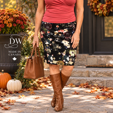 Load image into Gallery viewer, A woman wearing a coral pink top and a black knee-length floral skirt walks outdoors on a stone path with autumn leaves, holding a brown leather handbag. The image features a 'DW Made in Canada' logo overlay on the left.
