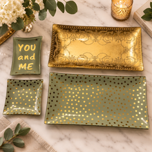 Load image into Gallery viewer, A set of four rectangular ceramic serving trays in sage green with gold accents, arranged on a white marble surface with decorative props including a candle, flowers, and books.
