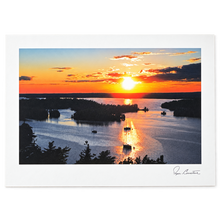 Load image into Gallery viewer, A landscape art print featuring a vibrant sunset over a lake with silhouetted islands and boats, presented with a wide white border and an artist signature in the bottom right corner.
