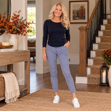 Charger l'image dans la galerie, A woman stands in a home entryway wearing a navy long-sleeve top and blue-and-white vertically striped ankle-length pants with white sneakers. The setting includes a staircase, console table, rug, and fall-themed decor.
