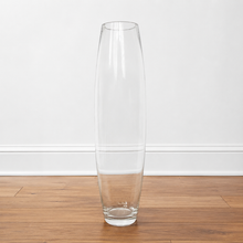Charger l'image dans la galerie, A tall, slender clear glass vase with a flared rim, standing on a wooden floor against a white wall.
